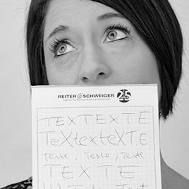 Eine Frau blickt nachdenklich auf und hält ein Klemmbrett mit handgeschriebenem Text in unterschiedlichen Größen und Ausrichtungen vor ihrem Mund.