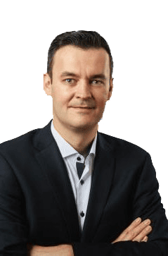 Eine Person mit kurzen dunklen Haaren trägt einen dunklen Anzug und ein helles Hemd und posiert mit verschränkten Armen und einem leichten Lächeln vor einem schlichten Hintergrund.