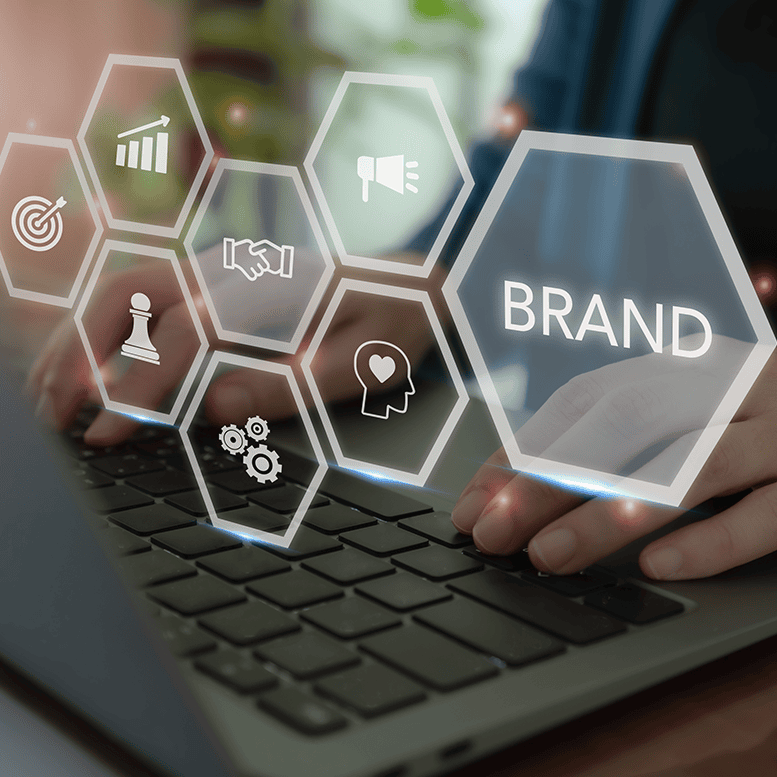 Hände tippen auf einer Laptoptastatur. Auf der digitalen Überlagerung sind Sechsecke mit Symbolen zum Thema Branding zu sehen, darunter Zielscheibe, Diagramm, Händedruck, Megafon, Schachfigur, Zahnräder und Herz. Das Wort „MARKE“ ist deutlich zu erkennen.