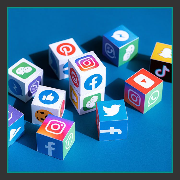 Bunte Würfel mit verschiedenen Social-Media-Logos, darunter Facebook, Instagram, Twitter und TikTok, sind auf einer blauen Oberfläche verstreut.
