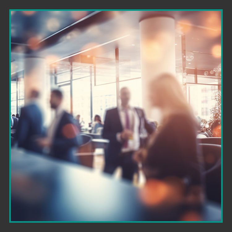 Unscharfes Bild von Menschen in einem modernen Büro oder Café mit großen Fenstern. Die Personen sind in kleinen Gruppen versammelt und scheinen sich zu unterhalten. Sanftes, warmes Licht schafft eine gemütliche Atmosphäre mit Bokeh-Effekt im Vordergrund.