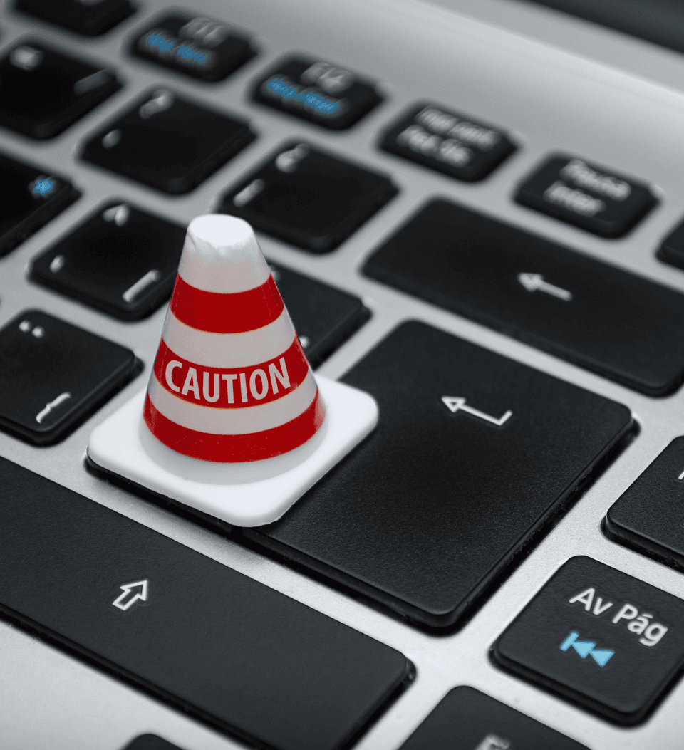 Ein kleiner orange-weißer Warnkegel sitzt in diesem Stock-Bild auf der Eingabetaste einer Computertastatur und symbolisiert eine Warnung oder einen Alarm im Zusammenhang mit der Computernutzung oder der Online-Sicherheit.