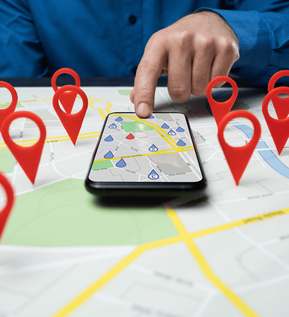 Die Hand einer Person zeigt auf ein Smartphone, das eine digitale Karte auf einer Papierkarte anzeigt, umgeben von roten Stecknadeln, die für Navigation und GPS-Technologie stehen.