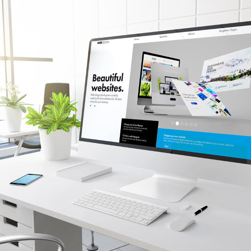 Ein moderner Büroarbeitsplatz mit einem großen Computermonitor, auf dem eine Webdesign-Seite mit Texten von Beautiful Websites angezeigt wird. Auf einem weißen Schreibtisch stehen Tastatur, Maus, Notizblock und eine Topfpflanze. Daneben steht ein Smartphone. Helles Tageslicht durchflutet den Raum.